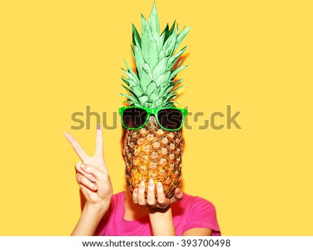 Fashion portrait of woman covering her face with pineapple with sunglasses over a yellow background Royalty-Free Stock Photo #393700498