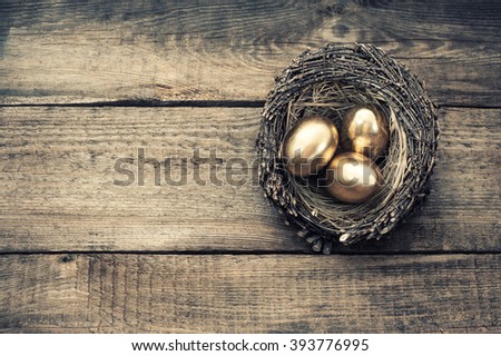 Golden easter eggs in birds nest on wooden background. Vintage style toned picture