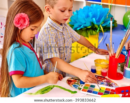 Girl and boy painting by brush on table in  kindergarten . 
