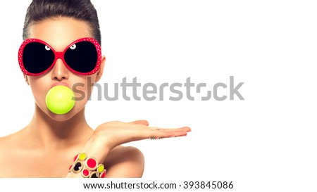 Beauty summer fashion model girl wearing sunglasses with green bubble of chewing gum and bright makeup showing empty copy space on the open hand palm for text over white background. Beautiful woman