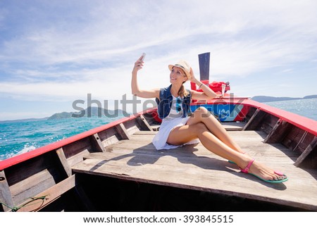 Happy vacation in Thailand. Pretty young woman taking selfie on smartphone sailing the sea on traditional longtail boat.