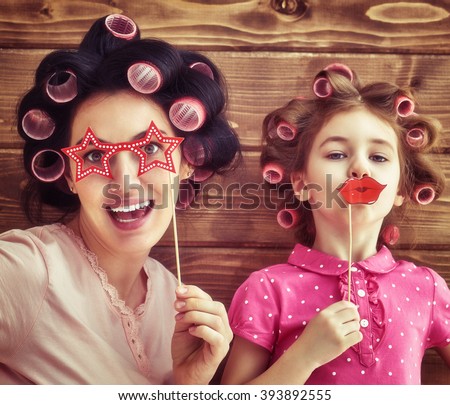 Funny family! Mother and her child daughter girl with a paper accessories. Beauty funny girl holding paper lips on stick. Beautiful young woman holding paper glasses on stick. Royalty-Free Stock Photo #393892555