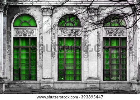 Facade of old abandoned building with three large arched windows of green glass. Monochrome background
