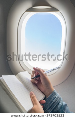 Woman writing on blank notebook while travelling on airplane.
