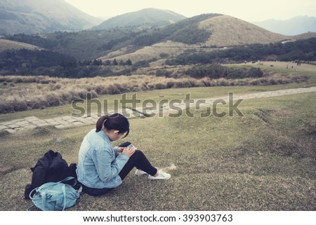 Woman using mobile phone while relaxing with mountain view. Vintage image processed.