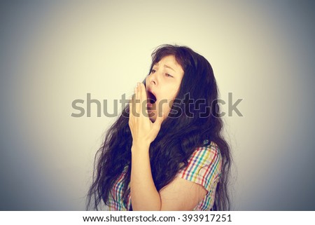Tired young brunette girl yawns. On gray background.