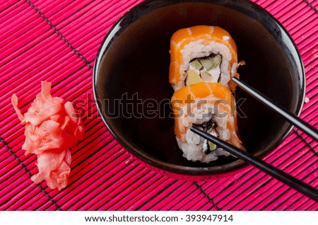 Sushi rolls in a black bowl, ginger and chopsticks (on a bright red bamboo background)