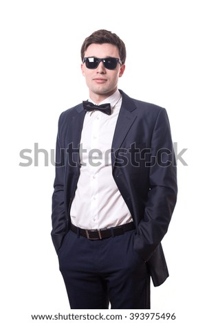 stylish young man in sunglasses, bow tie, dark suit and white shirt standing isolated on white background 