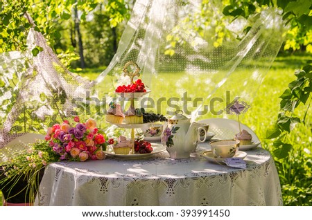 on the summer table with white tablecloth is set with white dishes cups and teapots from the tales of Alice with flowers and cakes