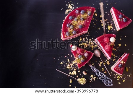 Pieces of delicious raspberry cake with fresh strawberries, raspberries, blueberry, currants and pistachios on black background. Free space for your text.
