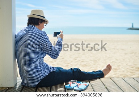 Rear side view of a man with smartphone sitting on a beach terrace on a sunny day outside background