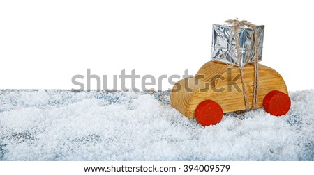 Wooden toy car with gift box on a snowy table over white ground