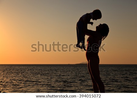 mother and little son play at sunset sky