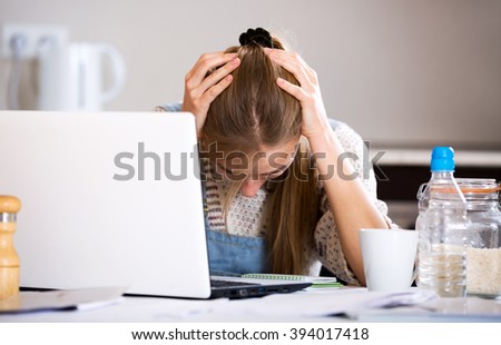 Portrait of unhappy young woman with laptop and documents indoors