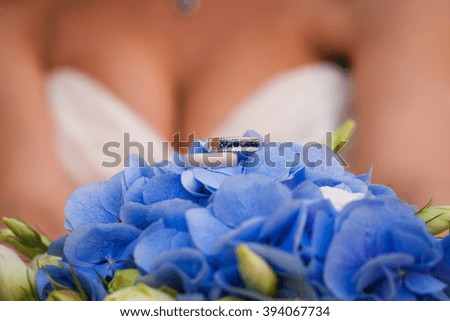 two wedding rings on the blue hydrangea. On the background is bride's decollete. One of the rings is with blue jewel