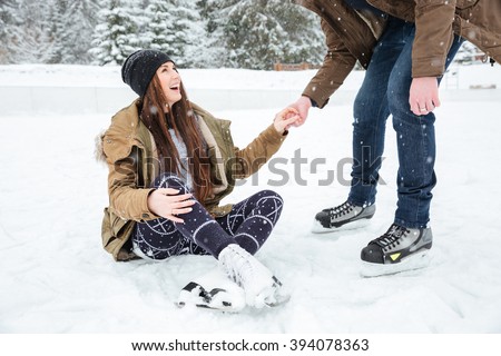 Man helping girl to stand on the ice rink outdoors