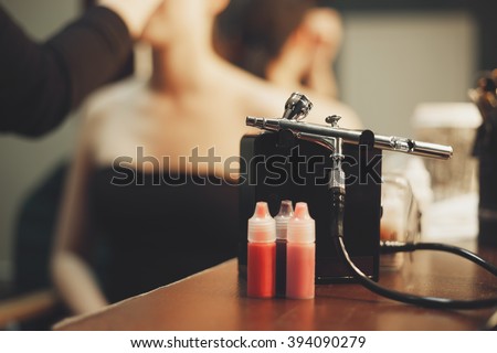 Makeup air brush.Paint brush for bodyart on visagist table with model painted on background.Airbrusher kit for body paint Royalty-Free Stock Photo #394090279
