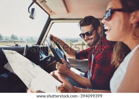Happy young couple with a map in the car. Smiling man and woman using map on roadtrip. Royalty-Free Stock Photo #394099399
