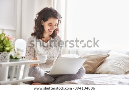 Happy casual beautiful woman working on a laptop sitting on the bed in the house. Royalty-Free Stock Photo #394104886