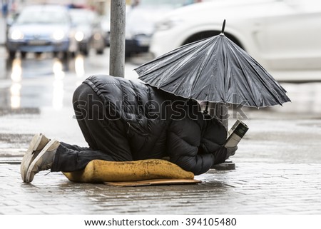 Homeless beggar is begging for money in a main street in Sofia holding an umbrella in a rainy day. Bulgaria is the poorest country in EU.