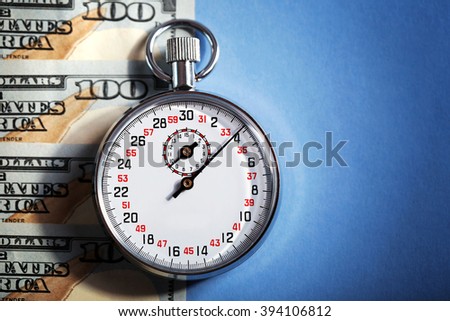 Stopwatch with dollar banknotes on blue background. Time is money concept