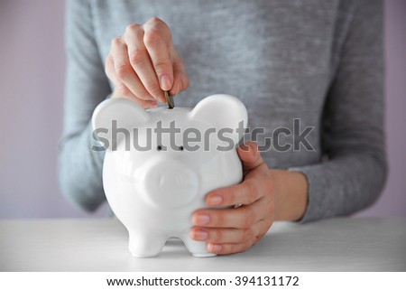 Woman putting coin into white piggy bank at the table