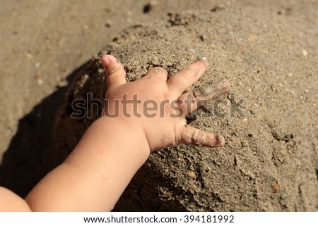 Closeup of one hand of small baby child playing with wet sea coast sand touching builded tower sunny day outdoor, horizontal picture