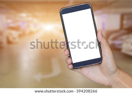  Man hand holding mobile smart phone,tablet,cellphone over Blur of backgrond with  parking area with perspective view,blur image with bokeh of Car park interior for background usage.vintage photo