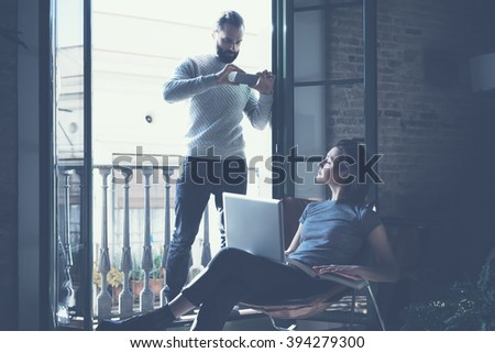 Young couple work together. Bearded man making photo smartphone beautiful girl. Working with new startup project in modern loft. Using contemporary notebook. Horizontal, film effect. 