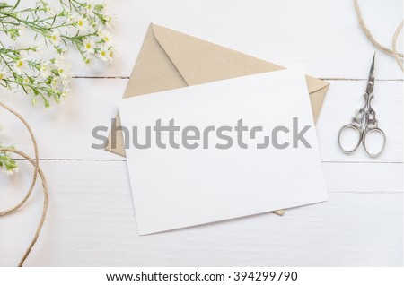 Blank white greeting card with brown envelop and daisy flowers on wooden table with vintage tone Royalty-Free Stock Photo #394299790
