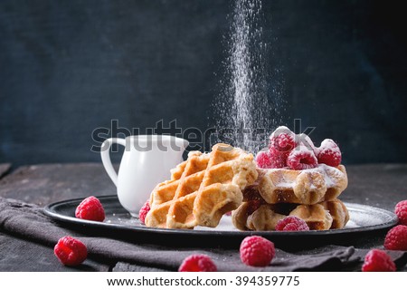 Belgian waffles with raspberries and sieving sugar powder, served with jug of milk on vintage metal tray with textile napkin over old wooden table. Dark rustic style. Royalty-Free Stock Photo #394359775