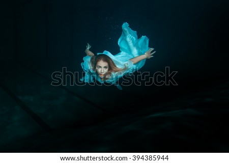 A woman in a white dress as a mermaid swimming under water. Royalty-Free Stock Photo #394385944