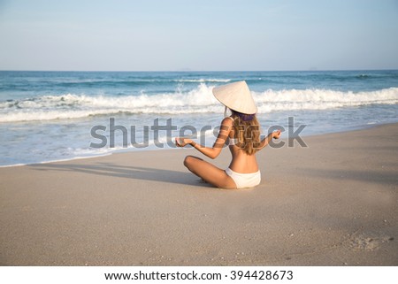 girl in the hat in the lotus position on the beach