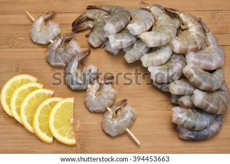 Many Raw Green King Size Shrimps or Prawns On Wooden Skewers With Yellow Lemon Slices On Wooden Background