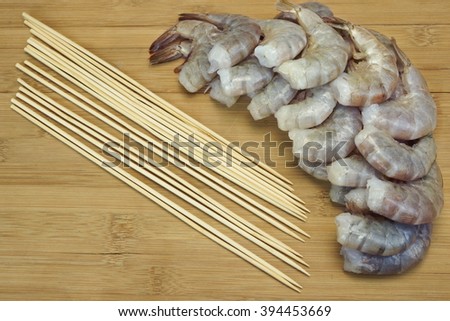 Many Raw Green King Size Shrimps or Prawns and Wood Skewers On Wooden Board Isolated