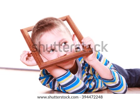 Spending free time and have fun. Playful little boy play with empty picture frame show face lie on floor.