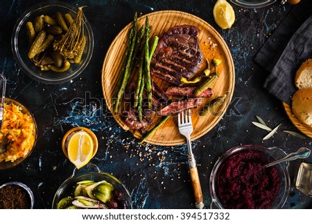 Fermented veggies and grilled meat concept. Sliced medium rare grilled beef barbecue Ribeye steak with chimichurri sauce, beet dip, red cabbage on cutting board on a dark food background. Royalty-Free Stock Photo #394517332