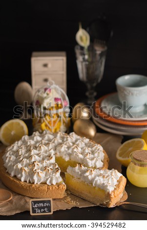 Lemon tart with meringue on a table with appliances on the black background
