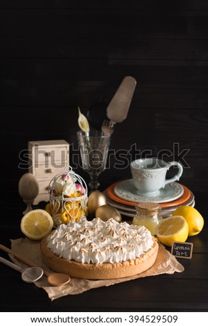 Lemon tart with meringue on a table with appliances on the black background
