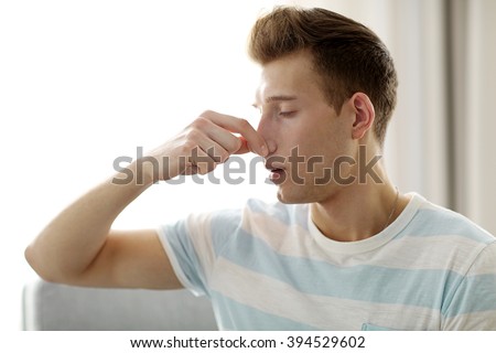 Young blonde man pinching his nose because of the stench in the room Royalty-Free Stock Photo #394529602