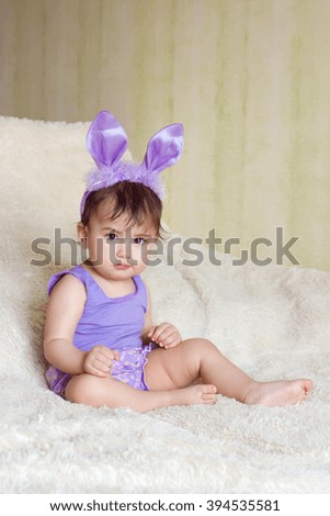 the child sits on the carpet in the purple Bunny suit