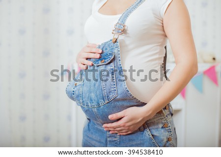 Belly of a pregnant woman in a blue denim overalls