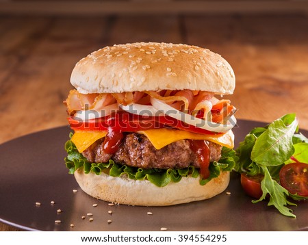 A juicy charcoal broiled hamburger with bacon, onion rings, tomato, cheddar cheese and vegetables.