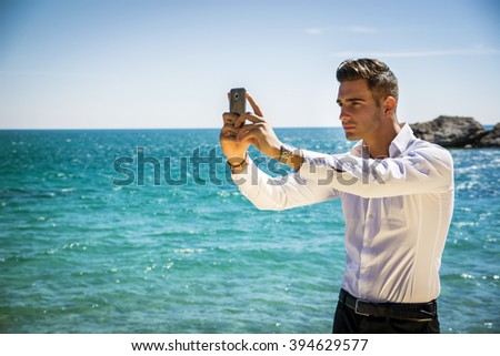 Side View of a Elegant Young Man Taking Selfie Photos at the Beach Standing, Under the Heat of the Sun.