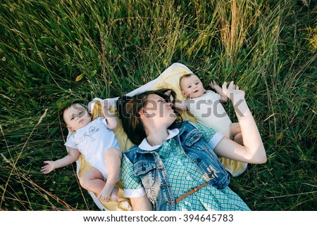 Portrait Of Happy young Family spending time outdoor on a summer day. Mother and Funny twins sisters newborn babies lying on grass  Royalty-Free Stock Photo #394645783