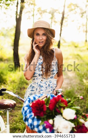 charming girl wearing dress and straw hat posing in park with vintage bicycle