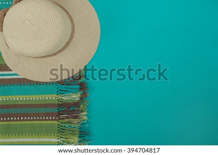 Straw hat and colorful striped cloth on a turquoise background. Top view. Horizontal image.