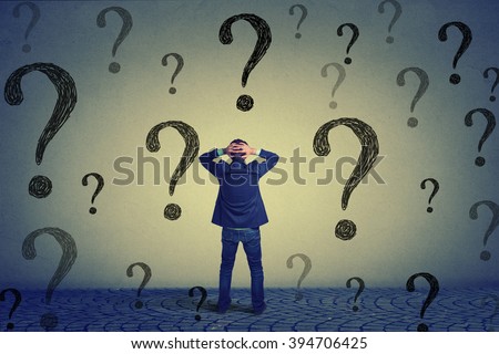 Rear view of young business man with hands on head standing in front of wall with many questions wondering what to do next. Full length of businessman facing the wall. Job work challenge concept  Royalty-Free Stock Photo #394706425