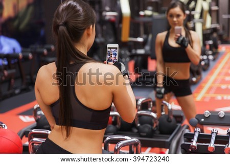 sport, fitness, lifestyle, technology and people concept - young woman with smartphone taking mirror selfie in gym