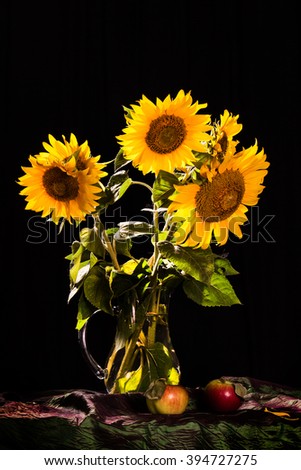sunflowers in a glass jug with apples on the black background

